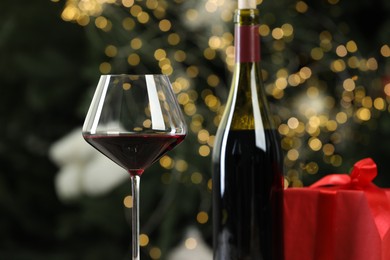 Photo of Glass and bottle of red wine against decorated Christmas tree, closeup