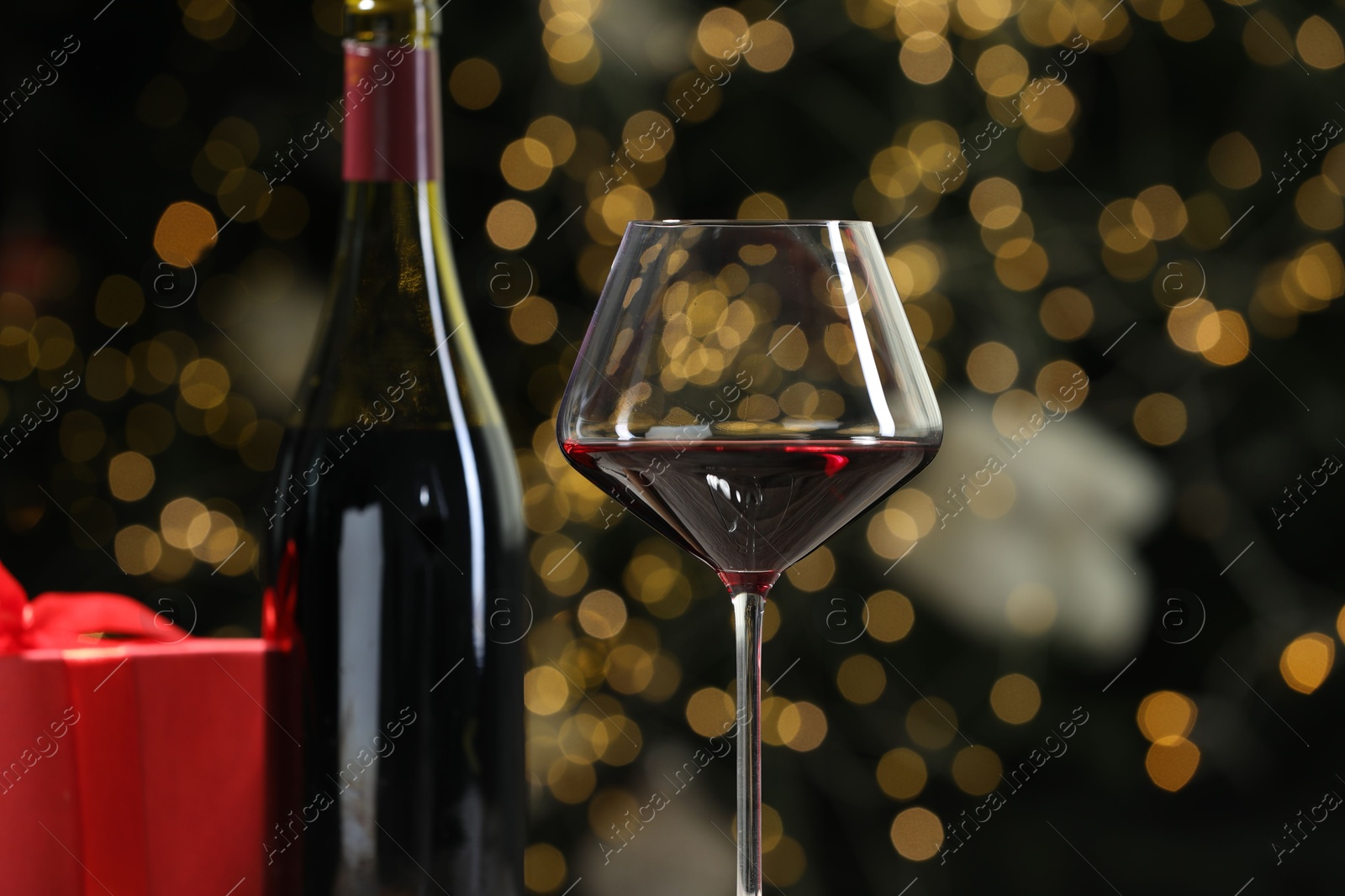 Photo of Glass and bottle of red wine against decorated Christmas tree, closeup