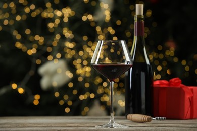 Photo of Red wine, gift box and corkscrew on wooden table against decorated Christmas tree. Space for text