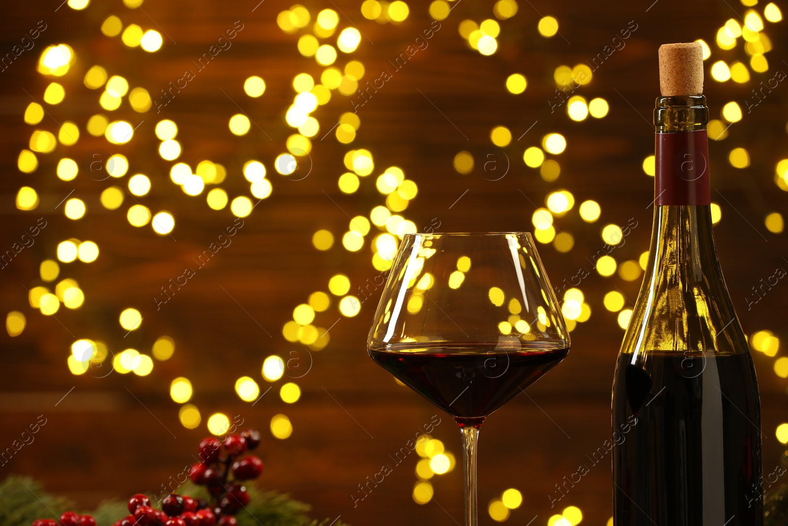 Photo of Glass and bottle of red wine against blurred Christmas lights, closeup