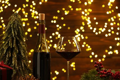 Photo of Red wine and Christmas decor against blurred lights, closeup