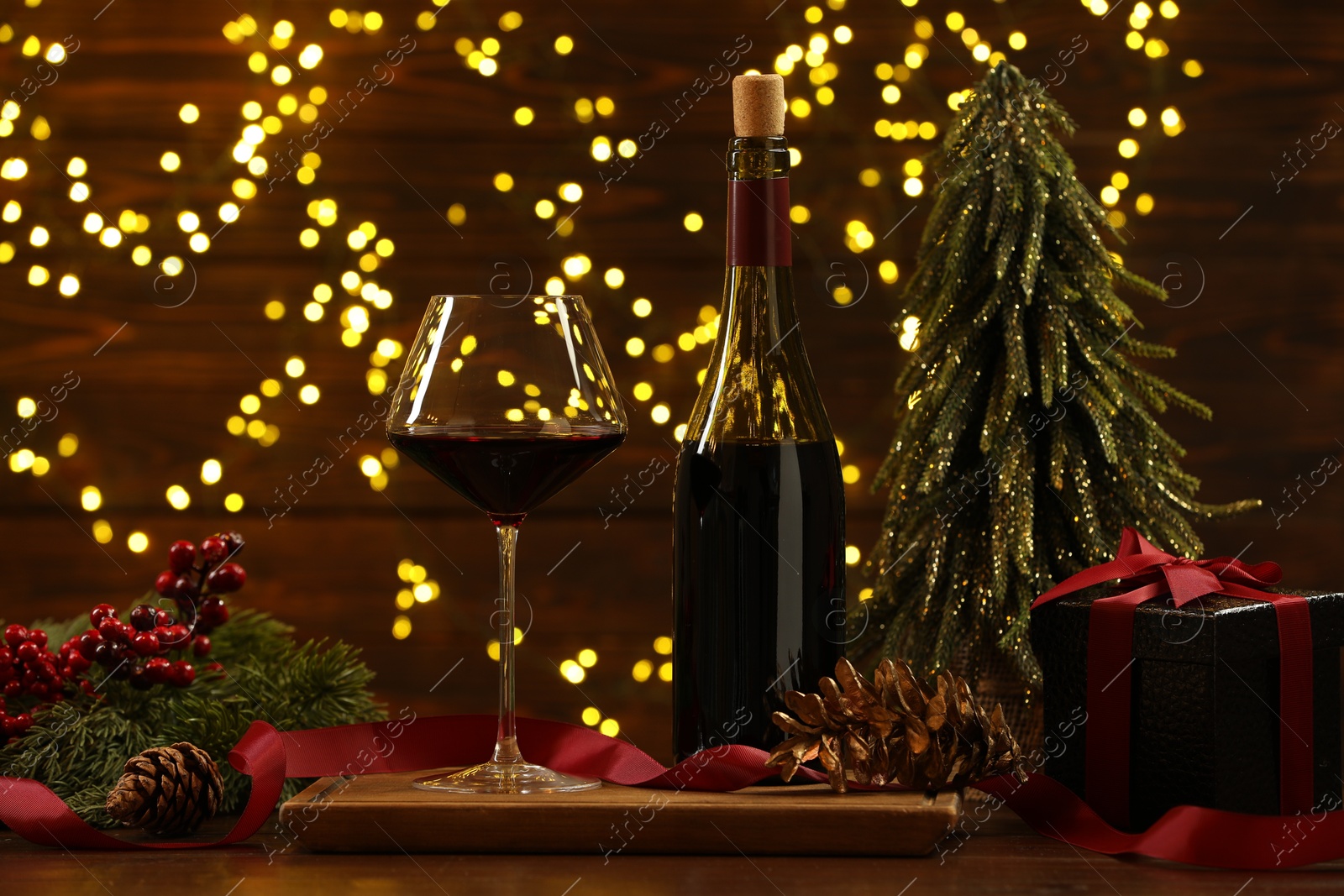 Photo of Red wine and Christmas decor on wooden table against blurred lights