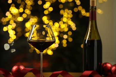 Photo of Red wine and Christmas decor on table against blurred lights, closeup