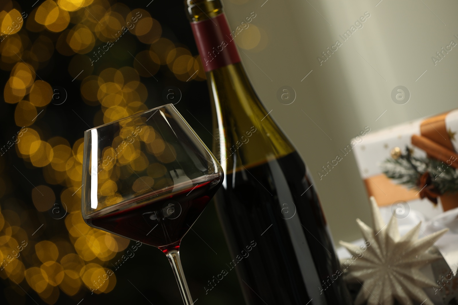 Photo of Glass and bottle of red wine against blurred Christmas lights, closeup