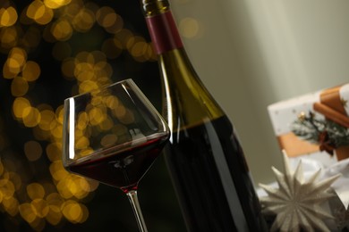 Photo of Glass and bottle of red wine against blurred Christmas lights, closeup