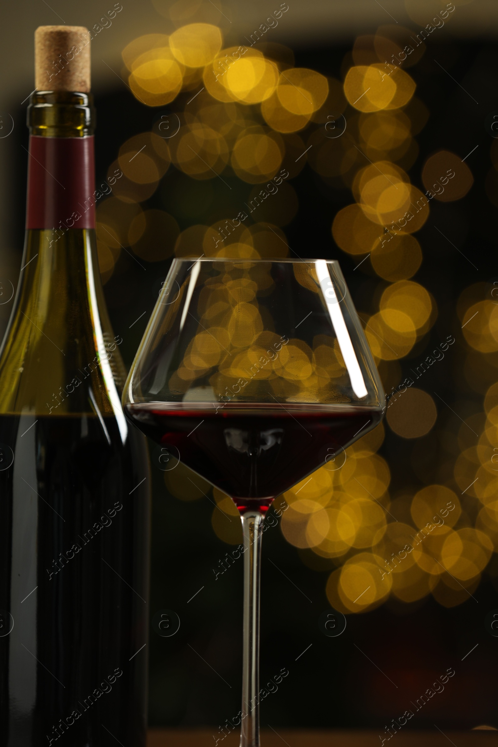 Photo of Glass and bottle of red wine against blurred Christmas lights, closeup