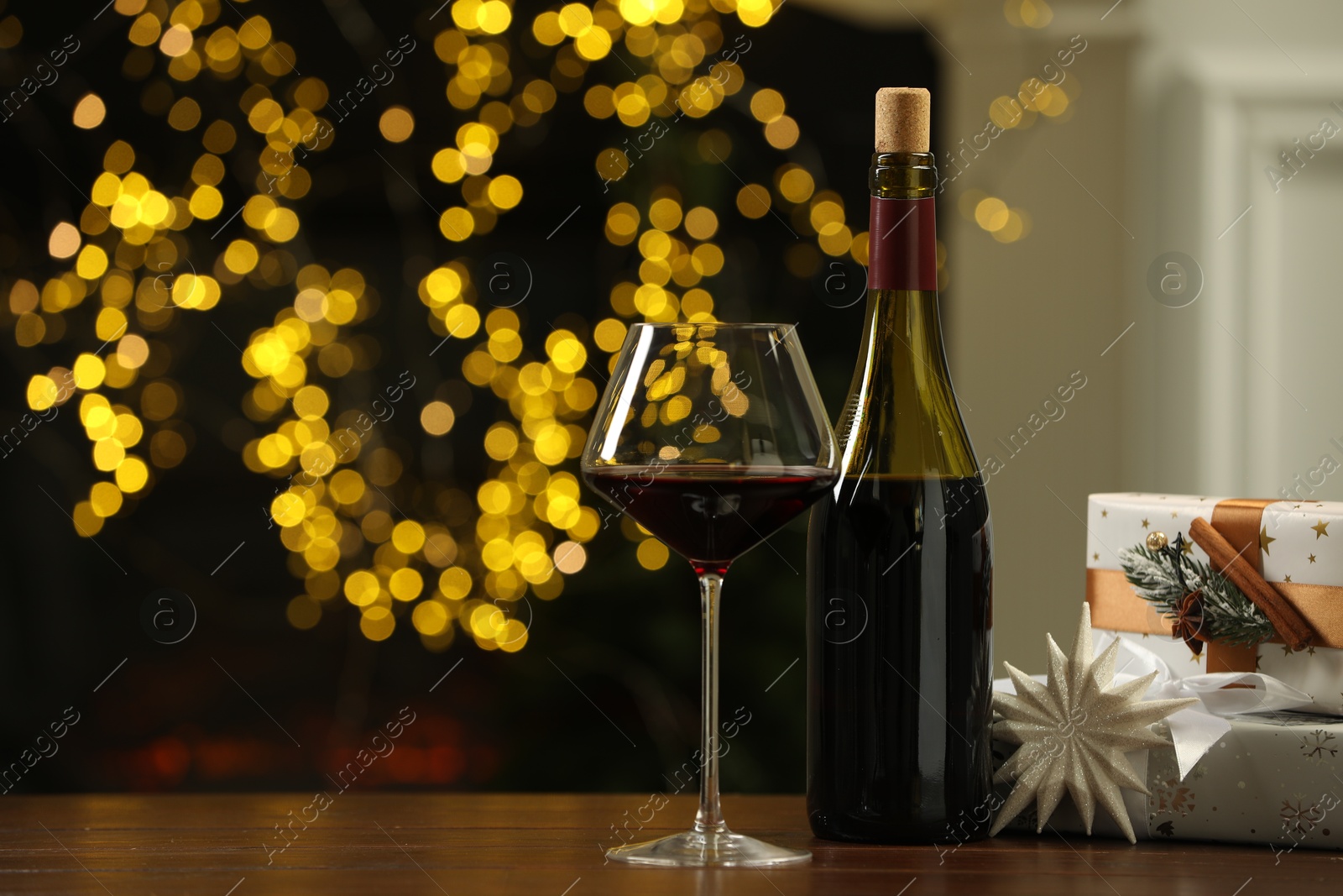 Photo of Red wine and gift boxes on wooden table against blurred Christmas lights. Space for text