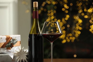 Photo of Red wine and gift boxes against blurred Christmas lights, closeup