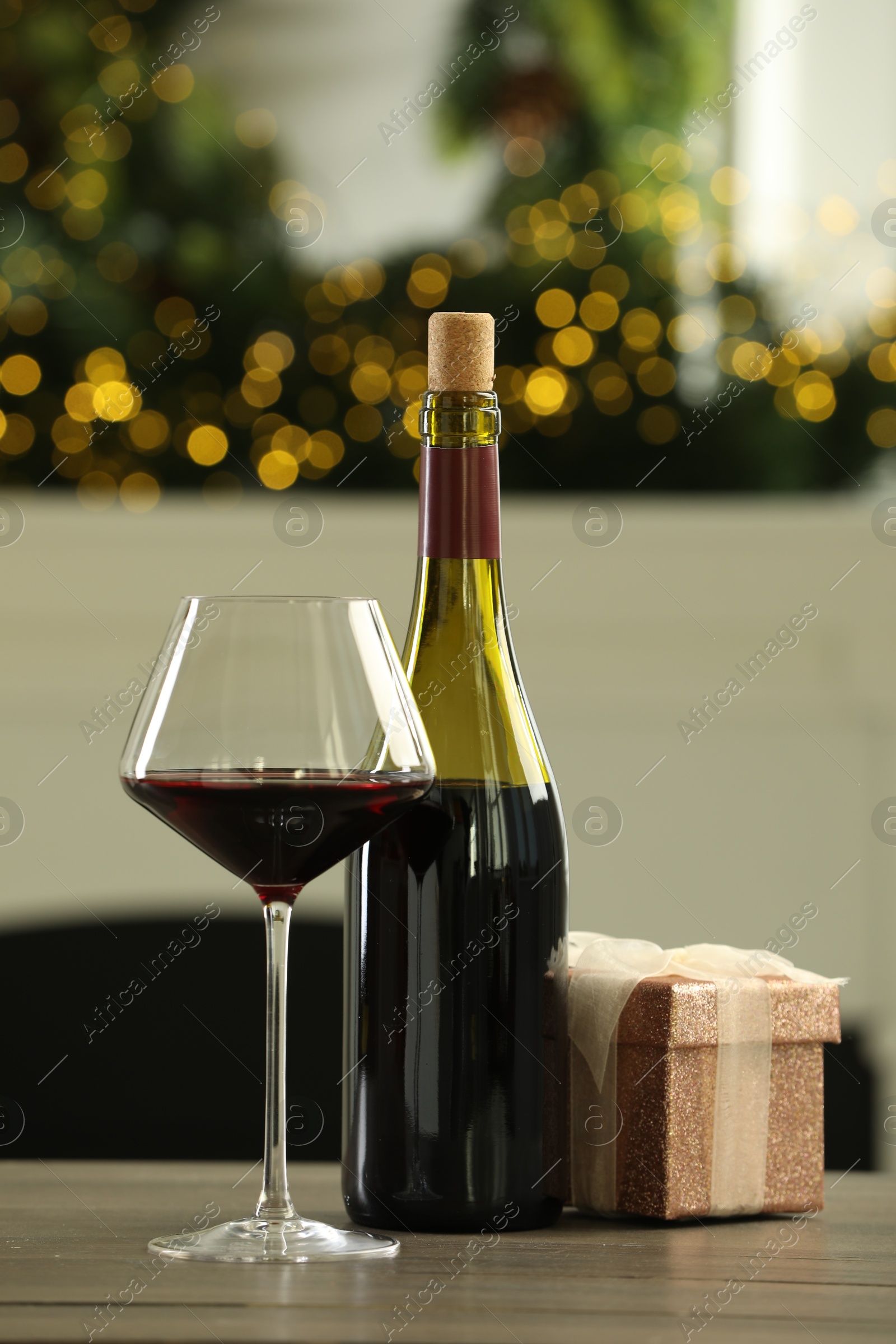 Photo of Red wine and gift box on wooden table against blurred Christmas lights