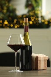 Photo of Red wine and gift box on wooden table against blurred Christmas lights