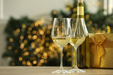 Photo of Glasses and bottle of white wine on wooden table against blurred Christmas lights. Space for text