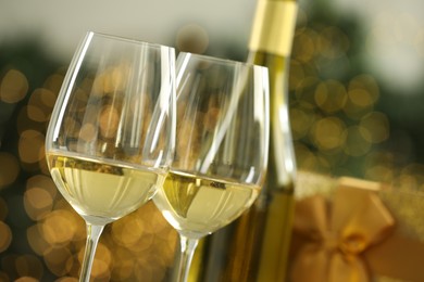 Photo of Glasses and bottle of white wine against blurred Christmas lights, closeup