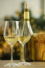 Photo of Glasses and bottle of white wine on wooden table against blurred Christmas lights, closeup