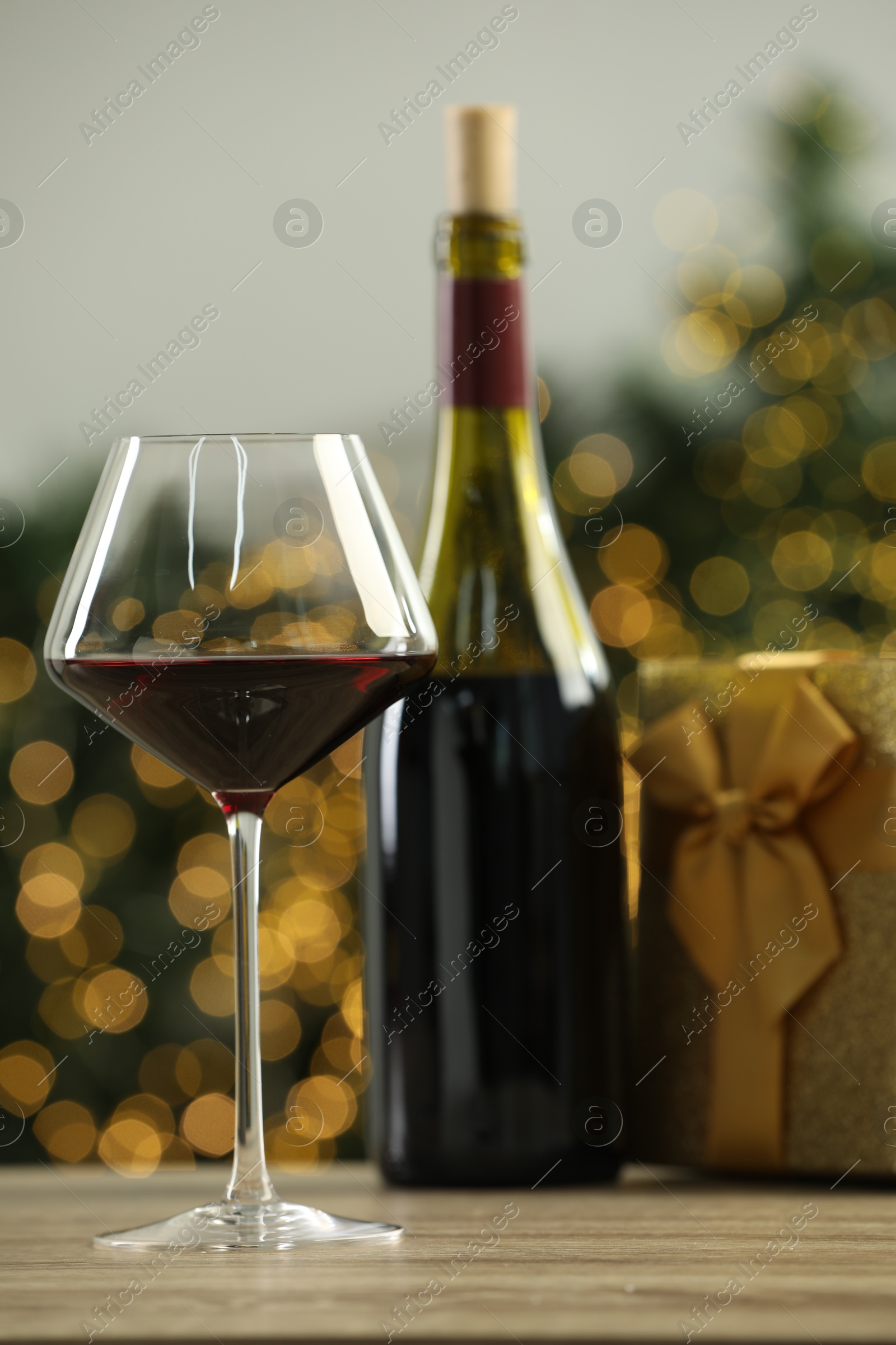 Photo of Red wine and gift box on wooden table against blurred Christmas lights