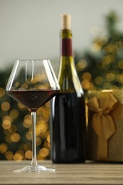 Red wine and gift box on wooden table against blurred Christmas lights