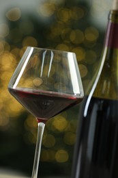 Glass and bottle of red wine against blurred Christmas lights, closeup