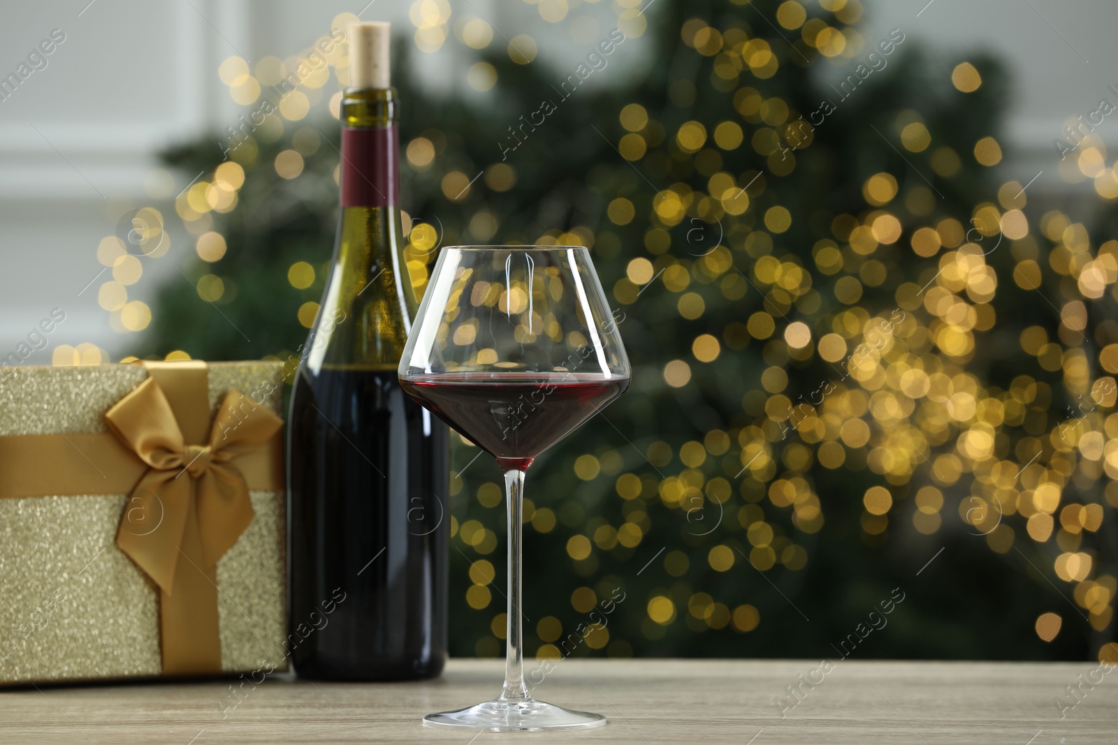 Photo of Red wine and gift box on wooden table against blurred Christmas lights. Space for text