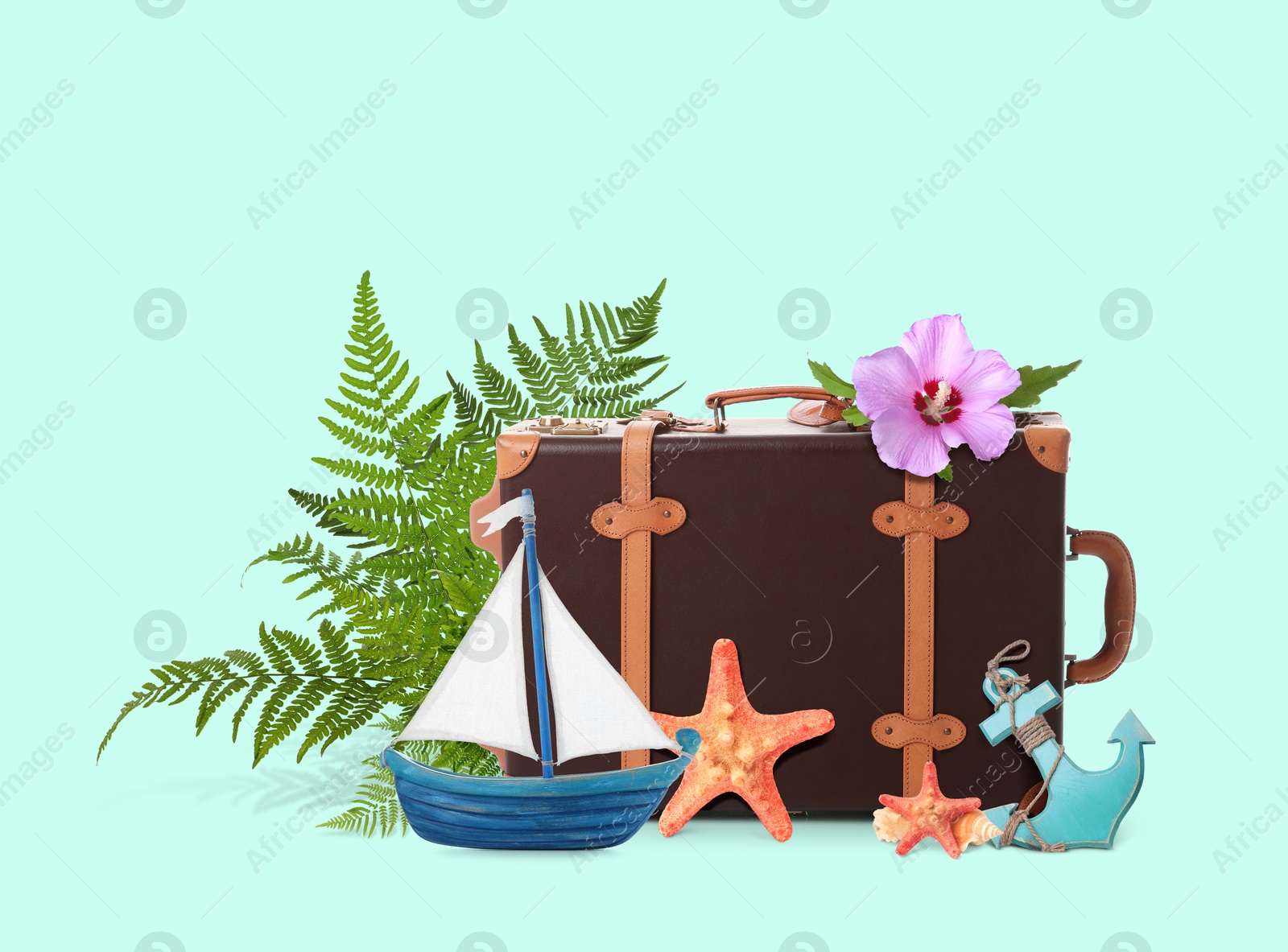 Image of Leather travel suitcase, toy sailboat and anchor, sea stars, tropical leaves and flower on turquoise background