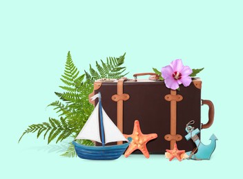 Image of Leather travel suitcase, toy sailboat and anchor, sea stars, tropical leaves and flower on turquoise background