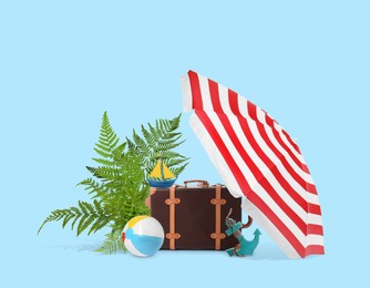 Leather travel suitcase, tropical leaves, toy sailboat and anchor, beach umbrella and ball on light blue background