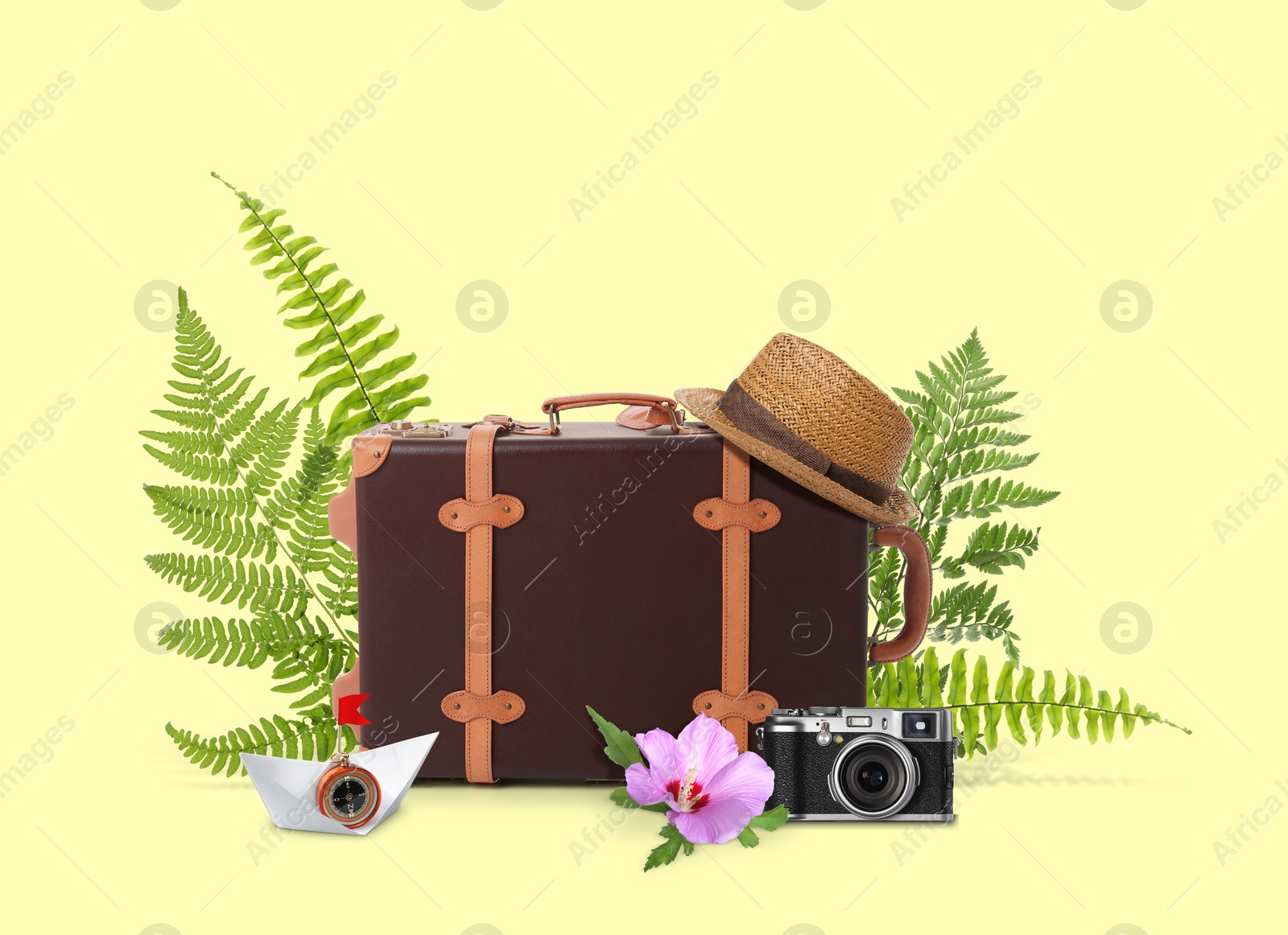 Image of Leather travel suitcase, paper boat with compass, hat, camera, tropical leaves and flower on light yellow background