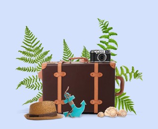 Image of Leather travel suitcase, toy anchor, camera, hat, seashells and tropical leaves on light blue background