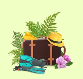 Image of Leather travel suitcase, hat, paper plane, swim fins, tropical leaves and flowers on light green background