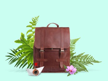 Image of Leather backpack, paper boat with compass, tropical leaves and flower on light turquoise background. Time to travel