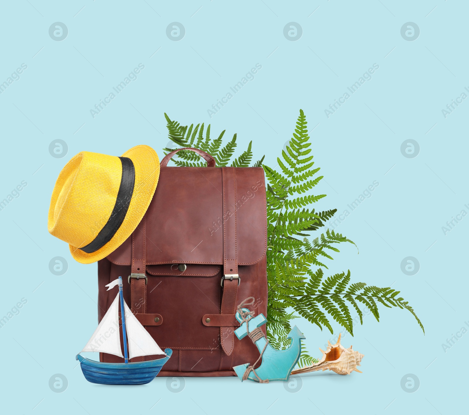 Image of Leather backpack, tropical leaves, hat, seashell, toy sailboat and anchor on light blue background. Time to travel