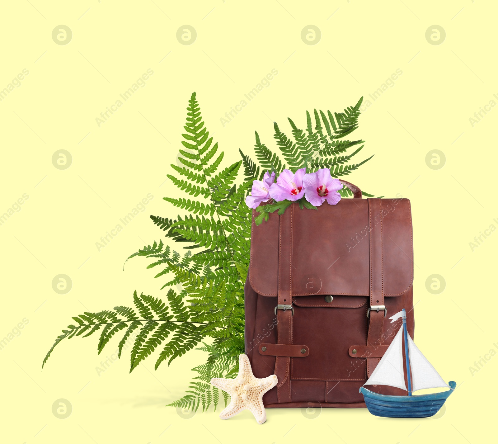 Image of Leather backpack, toy sailboat, sea star, tropical leaves and flowers on light yellow background. Time to travel