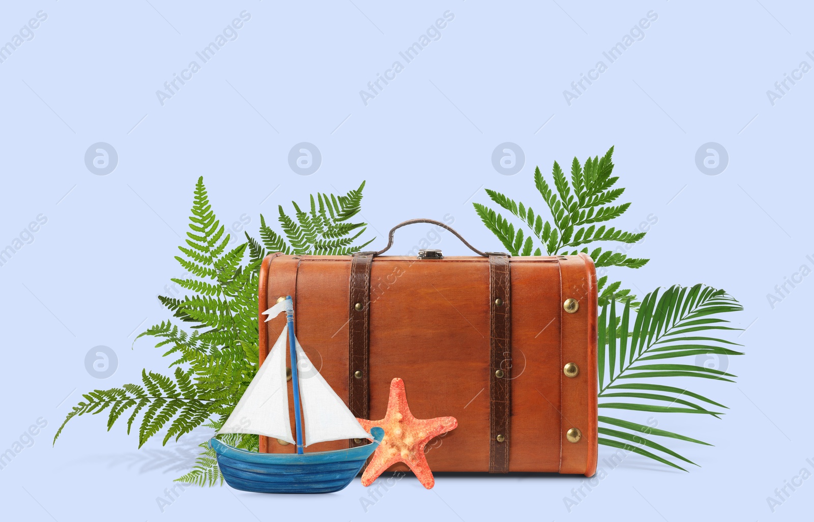 Image of Brown travel suitcase, tropical leaves, sea stars and toy sailboat on light blue background