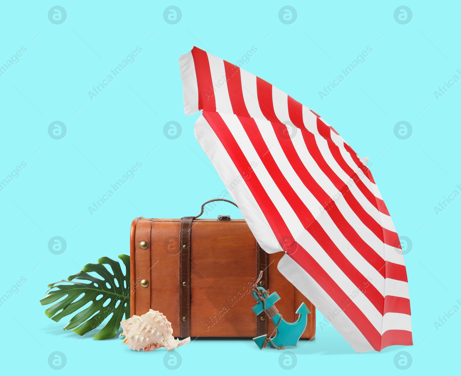 Image of Brown travel suitcase, tropical leaf, seashell, beach umbrella and toy anchor on cyan color background