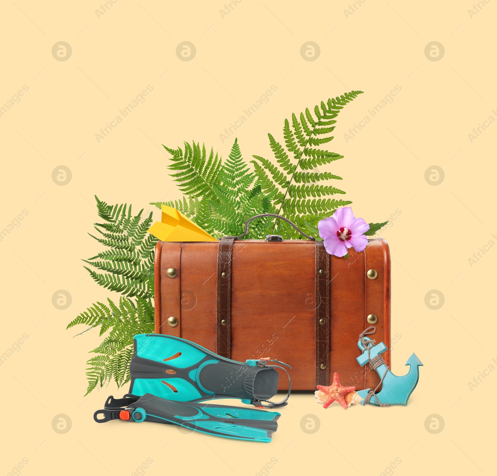 Image of Brown travel suitcase, paper plane, toy anchor, sea star, swim fins, tropical leaves and flower on beige background