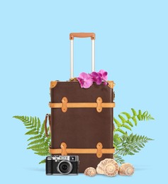 Image of Brown travel suitcase, seashells, camera, tropical leaves and flowers on light blue background