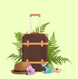 Image of Brown travel suitcase, hat, toy anchor, seashell, tropical leaves and flower on light green background