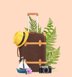 Image of Brown travel suitcase, hat, camera, toy sailboat, tropical leaves and flower on pink beige background