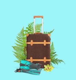 Brown travel suitcase, swim fins, tropical leaves and flower on cyan color background