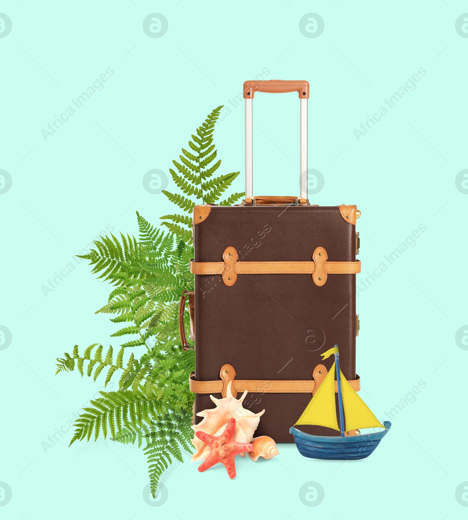 Image of Brown travel suitcase, tropical leaves, sea star, seashells and toy sailboat on light blue background