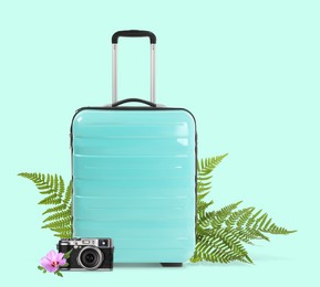 Image of Turquoise travel suitcase, camera, tropical leaves and flower on light blue background