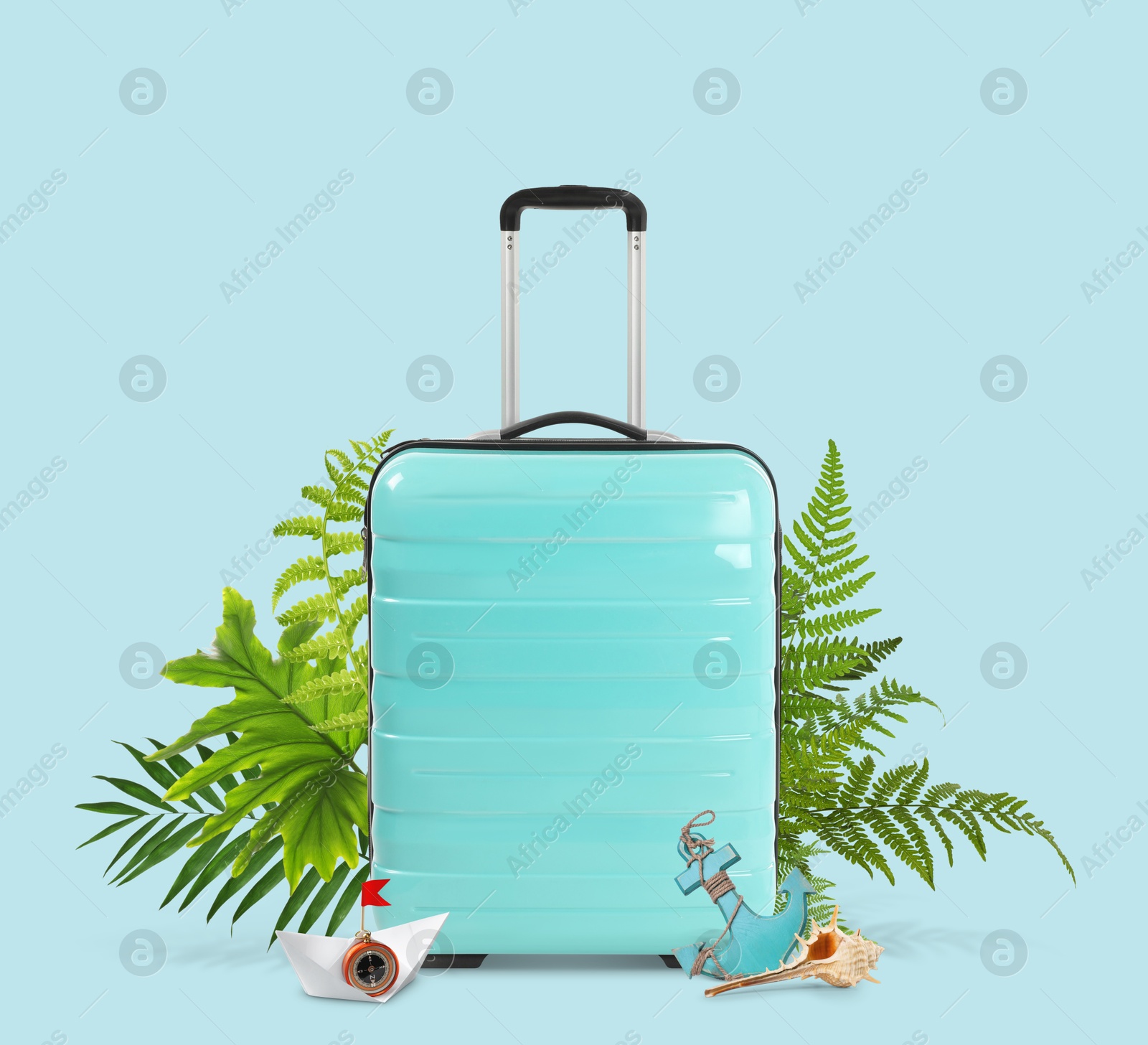 Image of Turquoise travel suitcase, tropical leaves, toy anchor, paper boat and seashell on light blue background