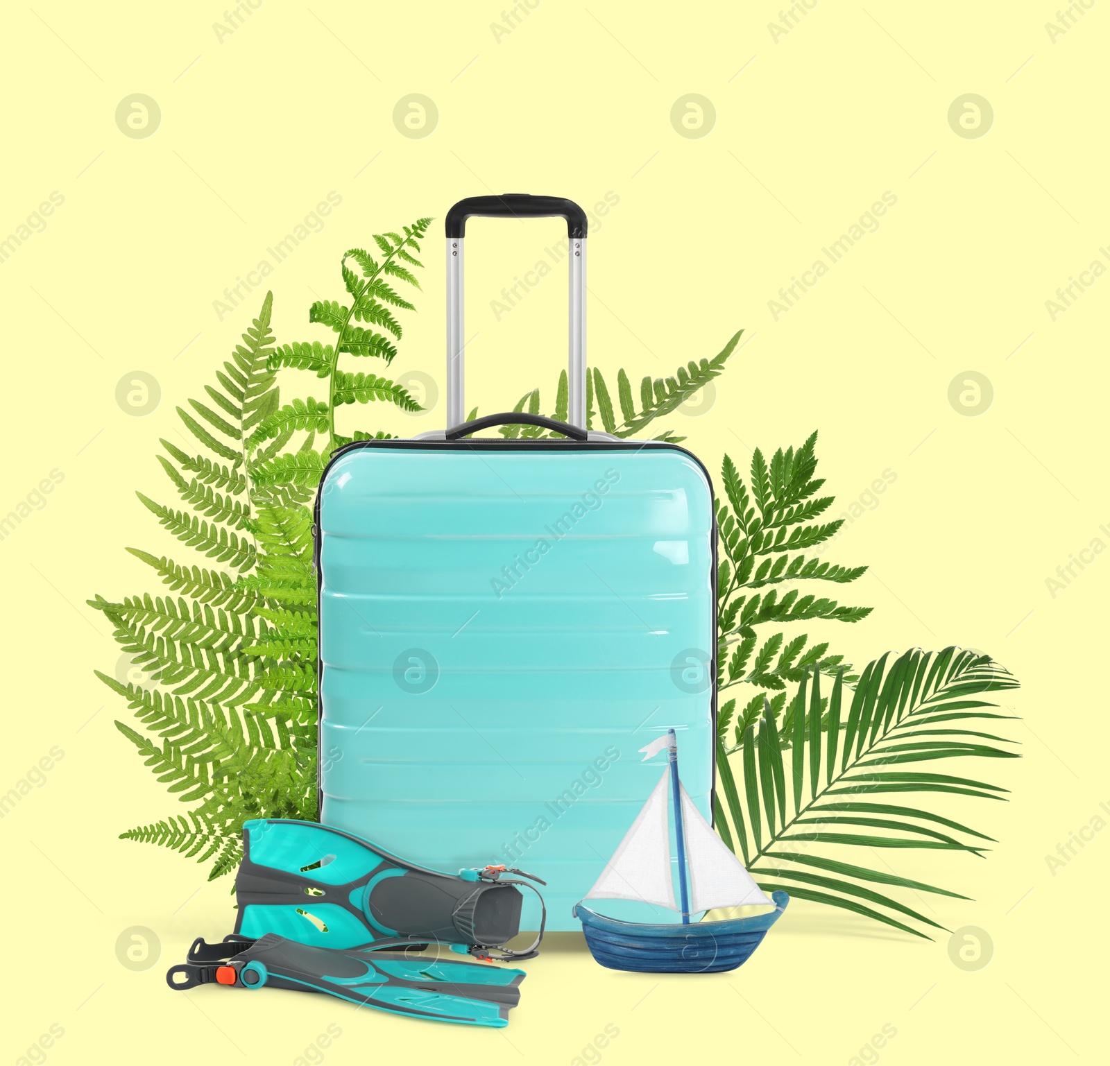 Image of Turquoise travel suitcase, tropical leaves, swim fins and toy sailboat on light yellow background