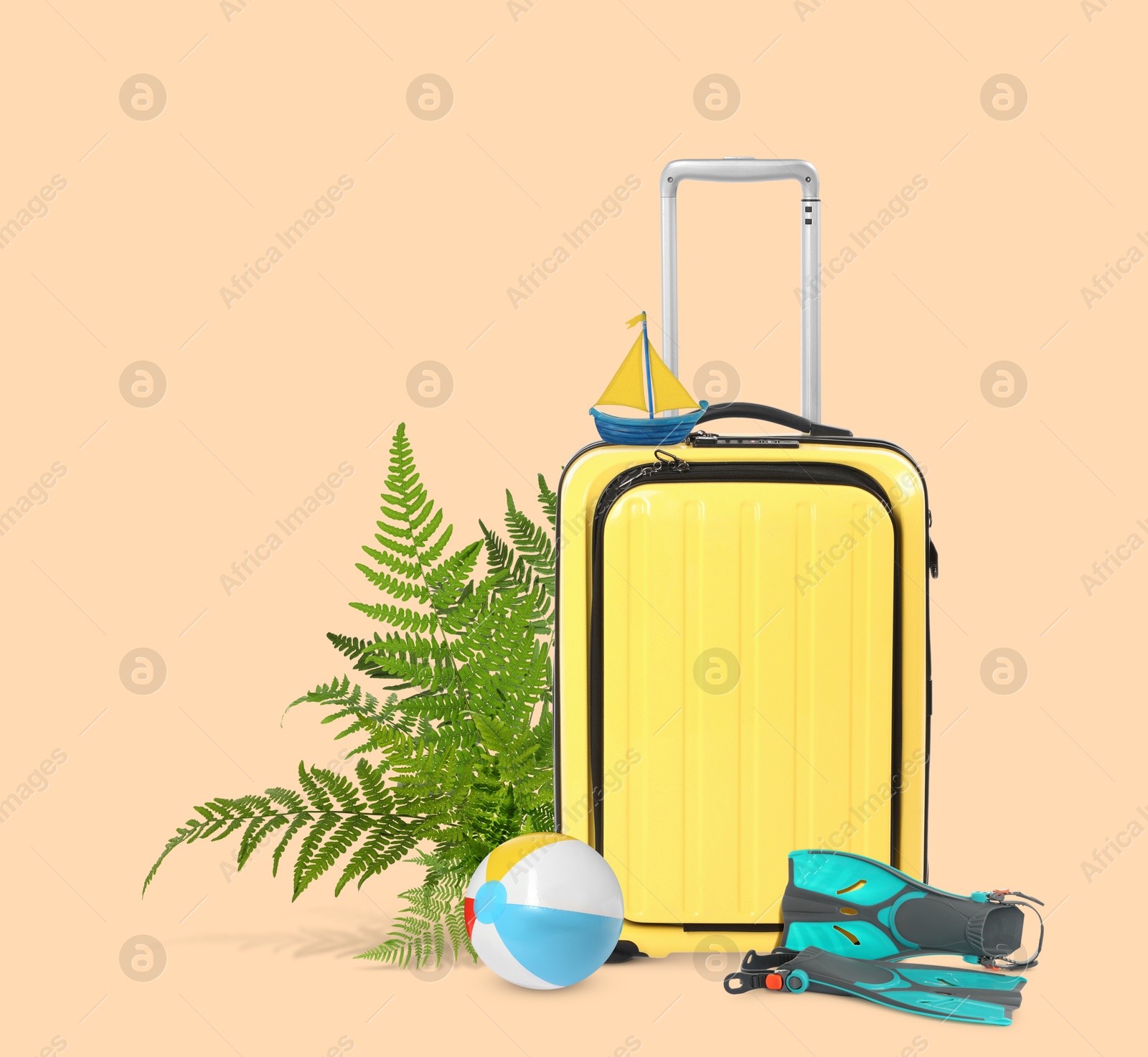 Image of Yellow travel suitcase, tropical leaves, swim fins, toy sailboat and beach ball on pink beige background