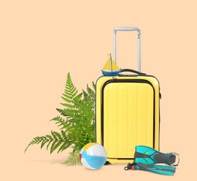 Image of Yellow travel suitcase, tropical leaves, swim fins, toy sailboat and beach ball on pink beige background