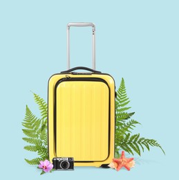 Image of Yellow travel suitcase, camera, sea star, seashell, tropical leaves and flower on light blue background