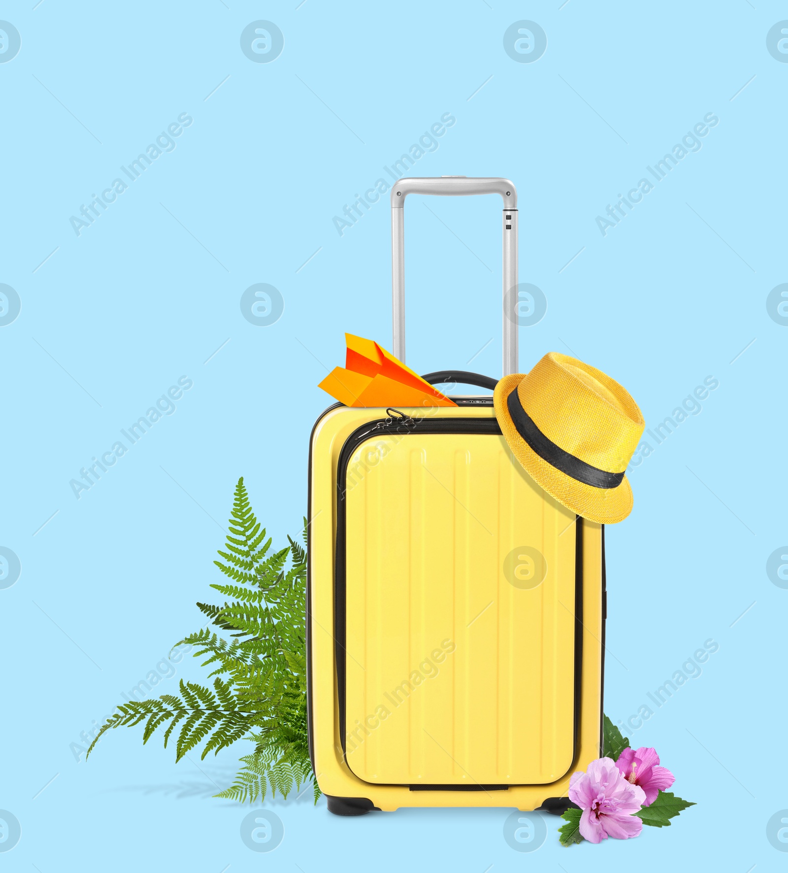 Image of Yellow travel suitcase, paper plane, hat, tropical leaves and flowers on light blue background