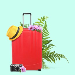 Image of Red travel suitcase, camera, hat, tropical leaves and flowers on light blue background