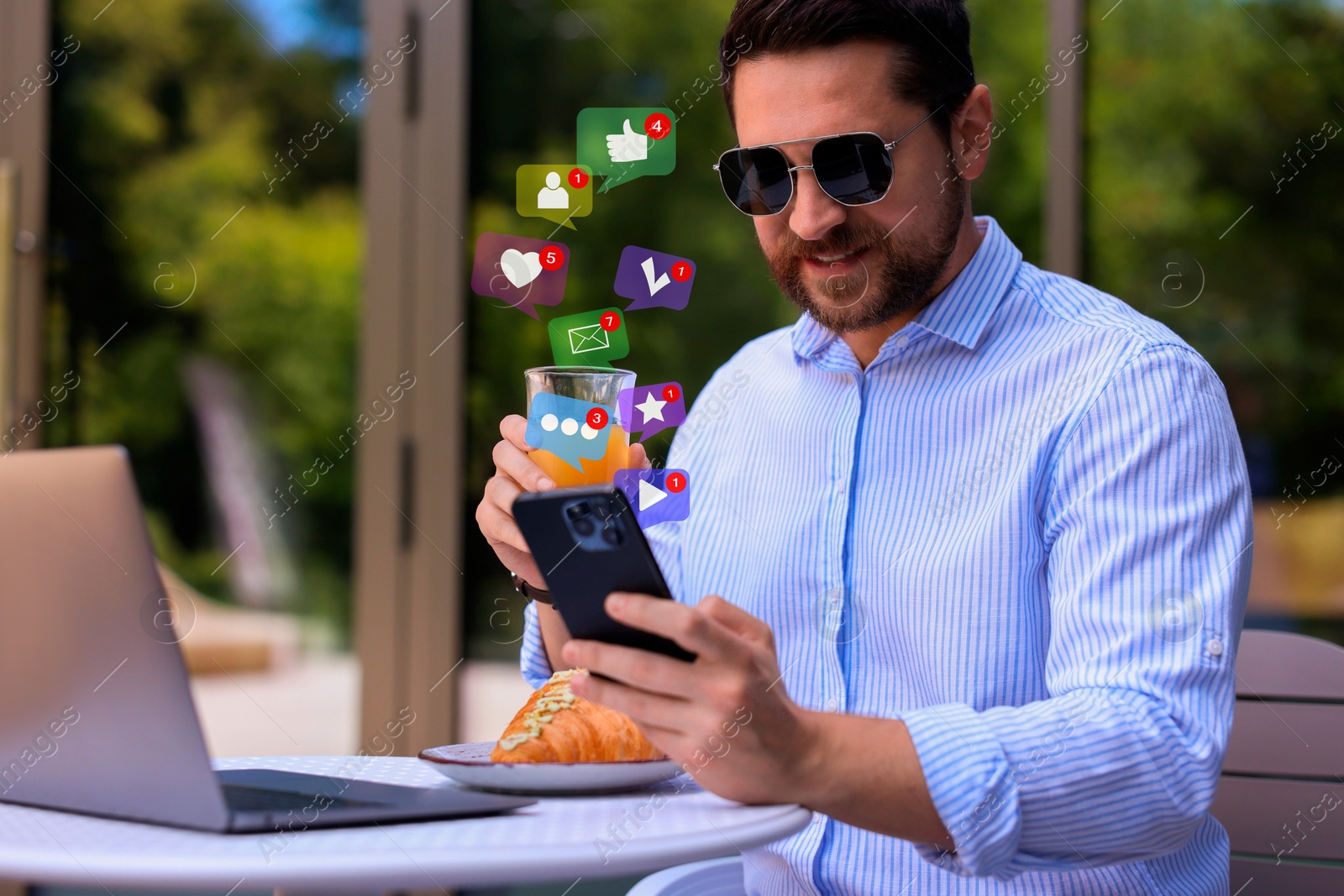 Image of Happy man using mobile phone while having break at outdoor cafe. New message sign and other notifications over gadget