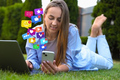 Image of Happy woman using mobile phone and laptop while lying on grass. New message sign and other notifications over gadget