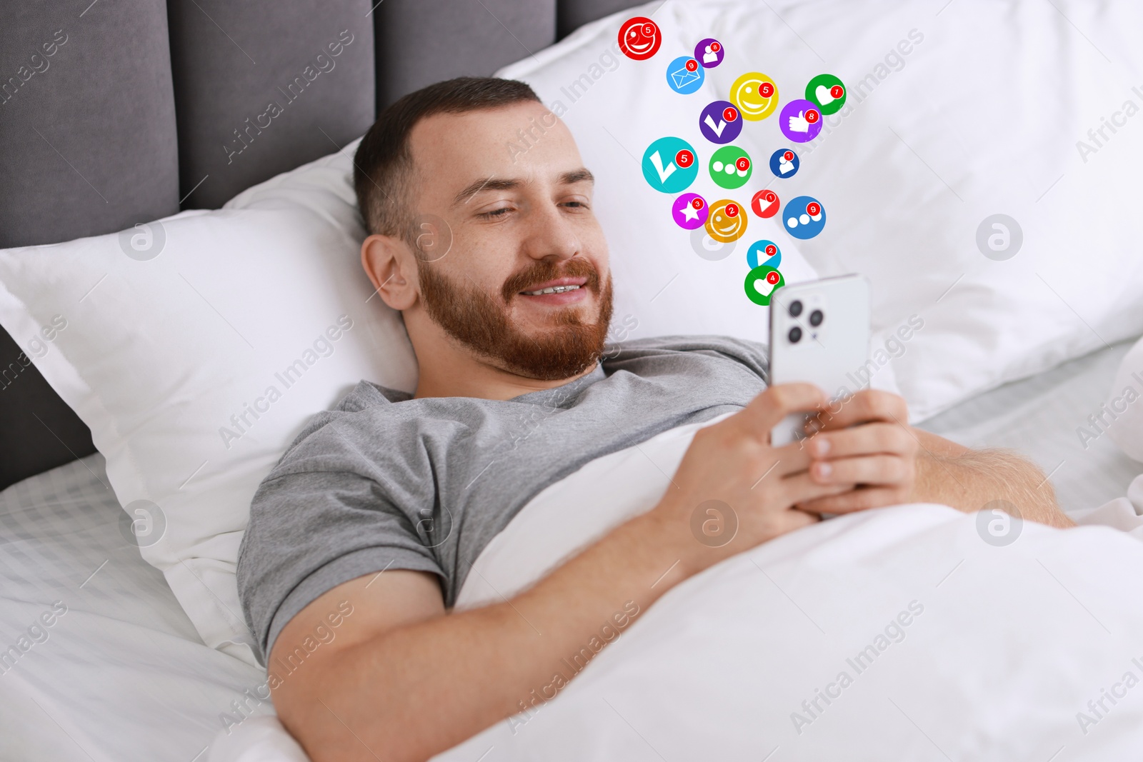 Image of Happy man using mobile phone in bed at home. New message sign and other notifications over gadget