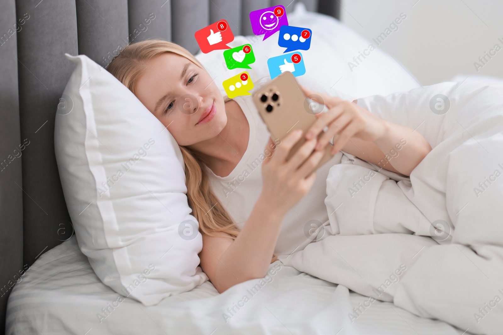 Image of Happy woman using mobile phone in bed at home. Different notification signs over gadget